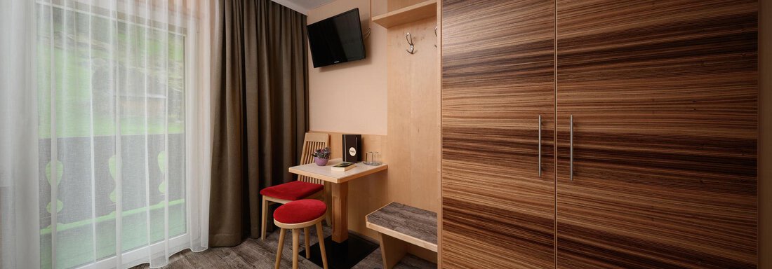 A modern room with a wooden wardrobe and a small desk. Soft light enters through the window, and the curtains are slightly open. - Haus Sonnschein - Zwieselstein