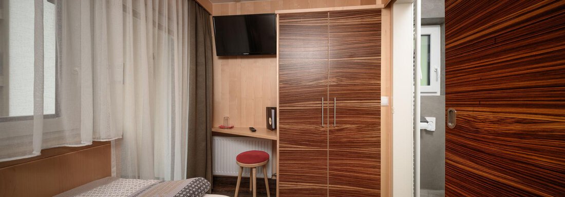 A modern room with a bed, a wooden wardrobe, and a desk. The room has large windows with curtains and pleasant lighting. - Haus Sonnschein - Zwieselstein