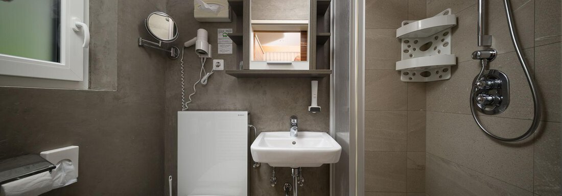 A modern bathroom with a shower, sink, and toilet. The walls are in neutral colors and there is storage space for toiletries. - Haus Sonnschein - Zwieselstein