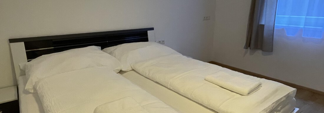 A cozy bedroom with two single beds and fresh linens. A window lets natural light in. - International House Sölden - Zwieselstein