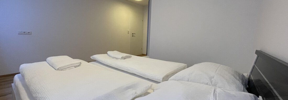 A simple bedroom with two single beds and fresh bed linens. The room features a bright wall design and a modern look. - International House Sölden - Zwieselstein