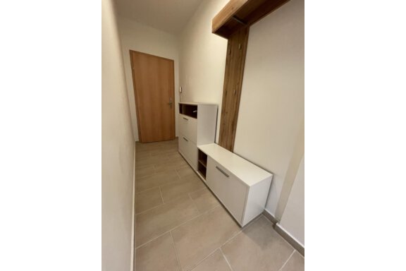 A bright hallway with a wooden area and modern white furniture. The walls are plain and the tiles are in neutral tones. - International House Sölden - Zwieselstein