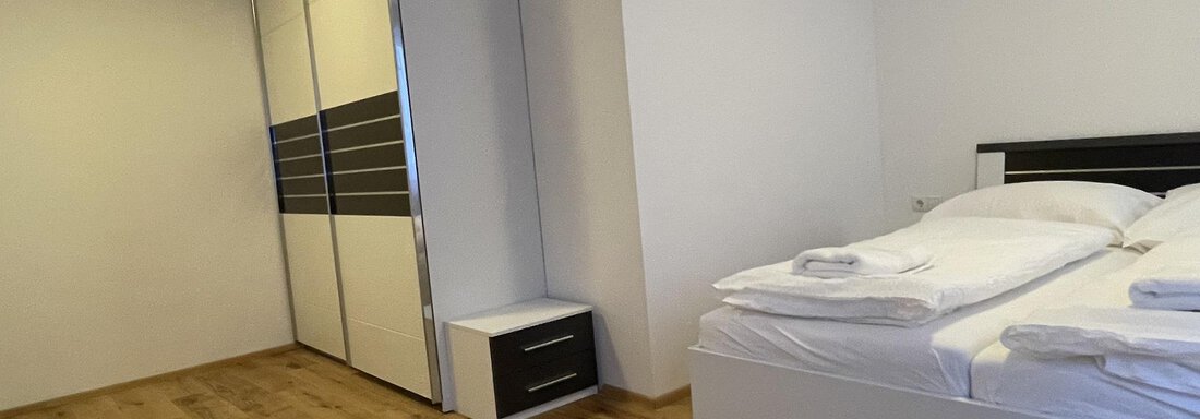 A simple and modern bedroom with a double bed and fresh bed linens. A large wardrobe and a bedside table complete the space. - International House Sölden - Zwieselstein