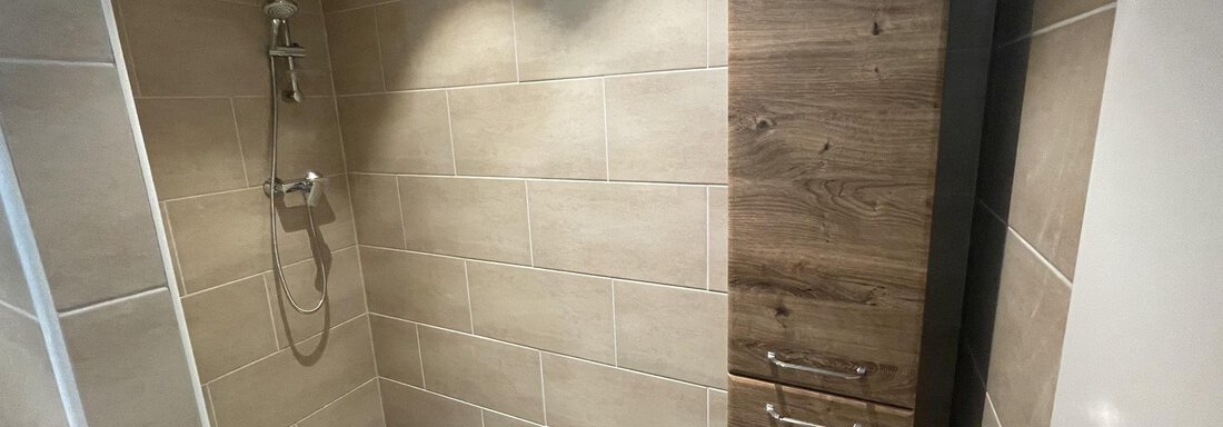 A modern shower with tiles in neutral colors. In the background, there is a wooden cabinet for towels and toiletries. - International House Sölden - Zwieselstein