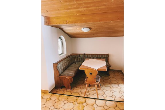 A cozy dining area with an upholstered corner bench and a small table. The walls are bright and the ceiling is made of wood, creating a warm atmosphere. - Landhaus Rosenhof - Zwieselstein
