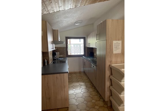 A modern kitchen with wooden furniture and bright tiles. It includes cooking appliances, a sink, and a window facing outside. - Landhaus Rosenhof - Zwieselstein