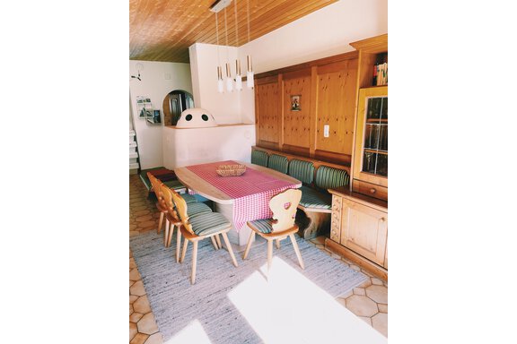 A cozy dining area with a large table and a checkered tablecloth. Around the table are wooden chairs, and there is a wooden bench against the wall. - Landhaus Rosenhof - Zwieselstein