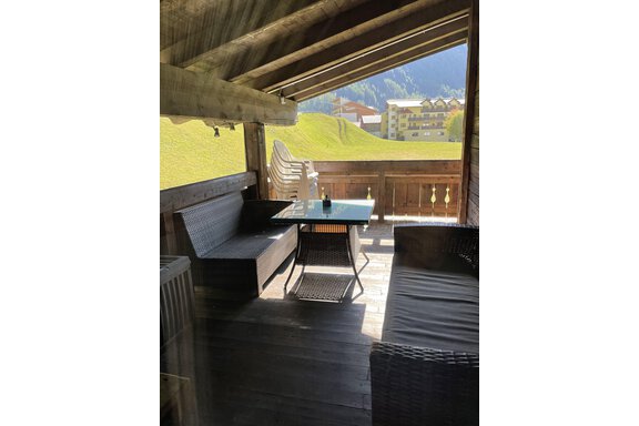 A cozy balcony with seating and a table. In the background, you can see green meadows and buildings. - Landhaus Rosenhof - Zwieselstein