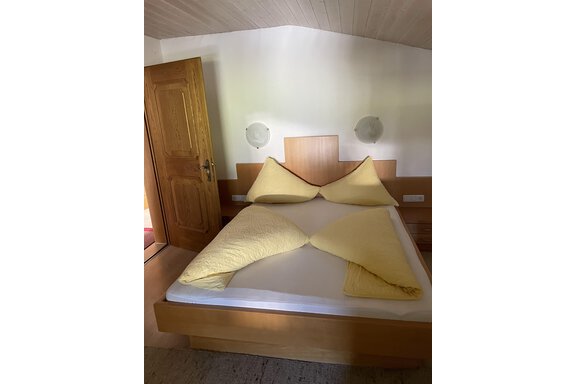 A cozy bedroom with a large bed and yellow pillows. The walls are bright and the room has a warm, inviting atmosphere. - Landhaus Rosenhof - Zwieselstein