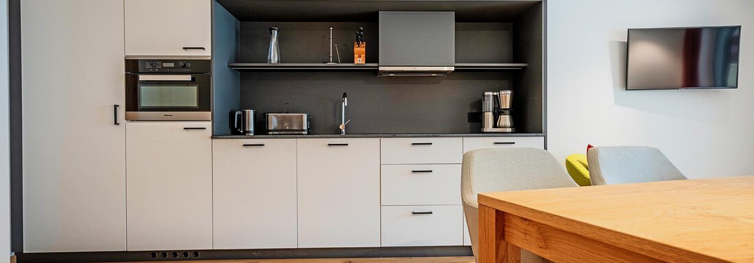Modern kitchen design with white cabinets and a dark countertop. A dining table and chairs complete the space. - Zwieselstein-Apart De Luxe - Zwieselstein