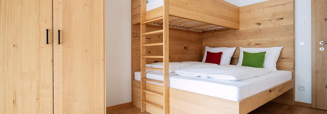 A modern bedroom with a wooden bunk bed and a cozy decor. The floor is made of light wood, and the room is bright and inviting. - Zwieselstein-Apart De Luxe - Zwieselstein