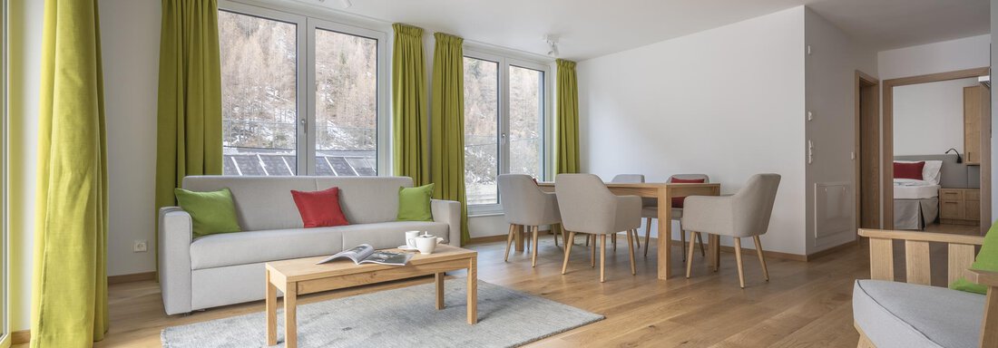 A modern living space with large windows and bright colors. A cozy sofa and a dining table invite relaxation and dining. - Zwieselstein-Apart De Luxe - Zwieselstein